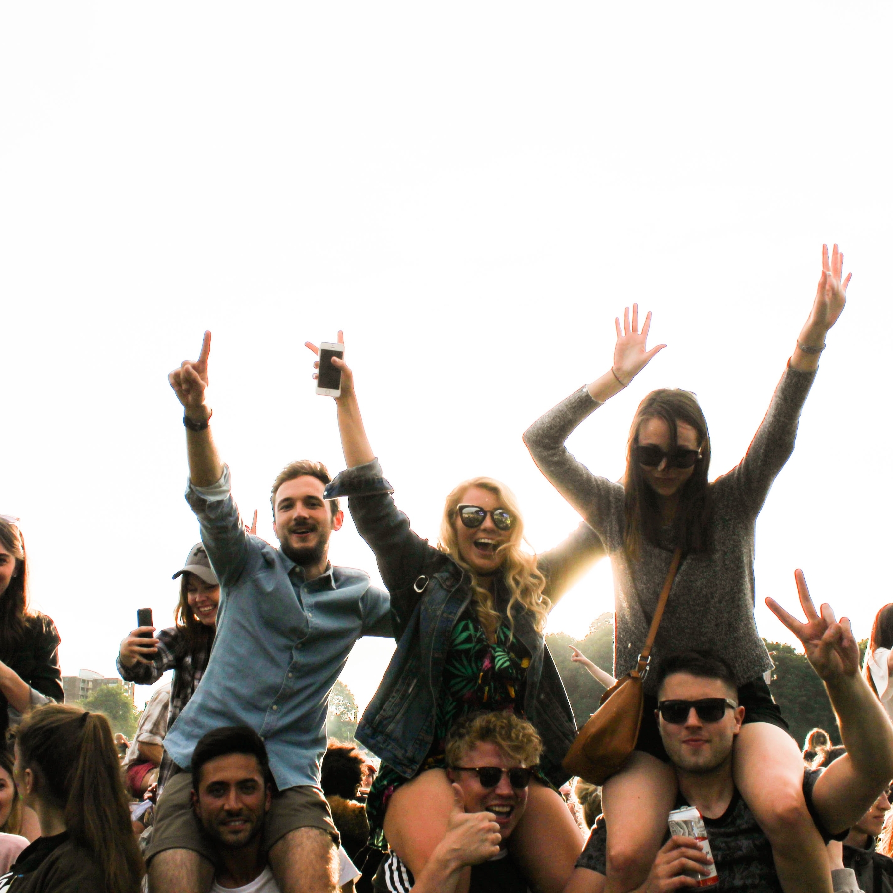 Concert goers seated on people's shoulders cheering in bright sunlight.